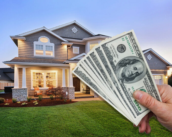 A man holding a few bills in front of a huge house